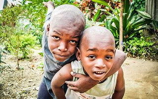 Annual International Service Trip Shines Light On Core Value Of Community 9 Two children, one with an arm around the other in an outdoor garden with green foliage, pose for a photo while looking at the camera, embodying the core value of community nurtured during their international service trip. Saint Joseph's College of Maine