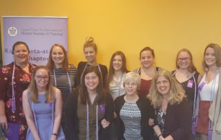 A group of nursing students, some wearing honor cords, pose in front of a sign for the Sigma Theta Tau International Honor Society, Kappa Beta-at-Large Chapter. Saint Joseph's College of Maine