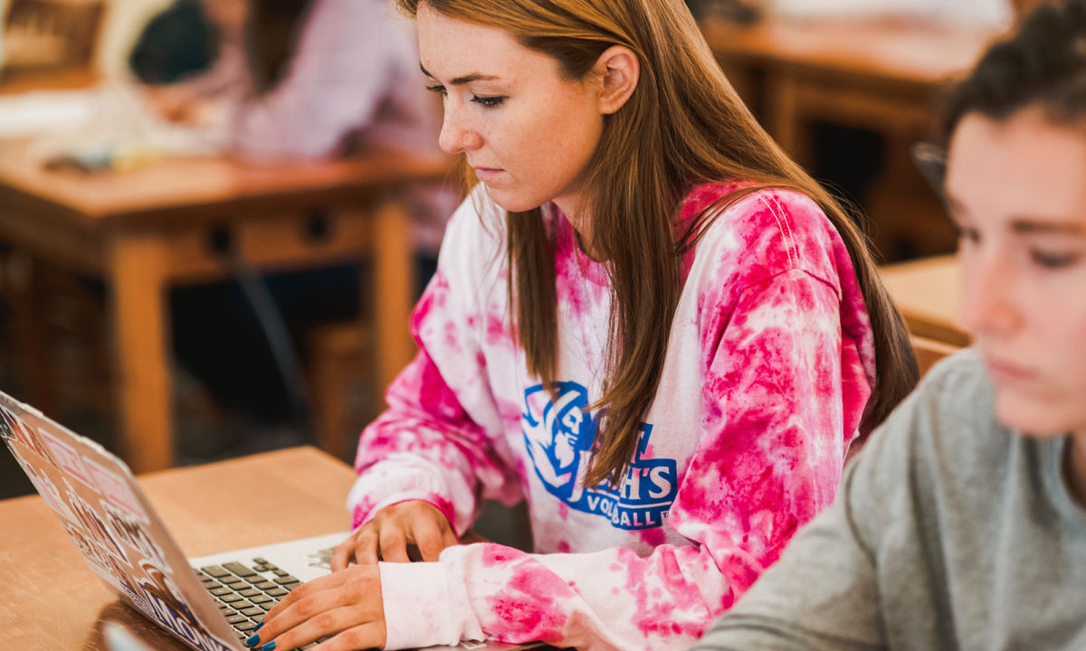 Business Programs 2 A person in a pink tie-dye shirt uses a laptop at a desk in a classroom setting. Saint Joseph's College of Maine