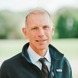 A woman with a bachelor in history, short, straight blond hair, wearing large gold earrings and a black top, smiles at the camera. Saint Joseph''s College of Maine