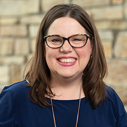 A woman with a bachelor in history, short, straight blond hair, wearing large gold earrings and a black top, smiles at the camera. Saint Joseph''s College of Maine