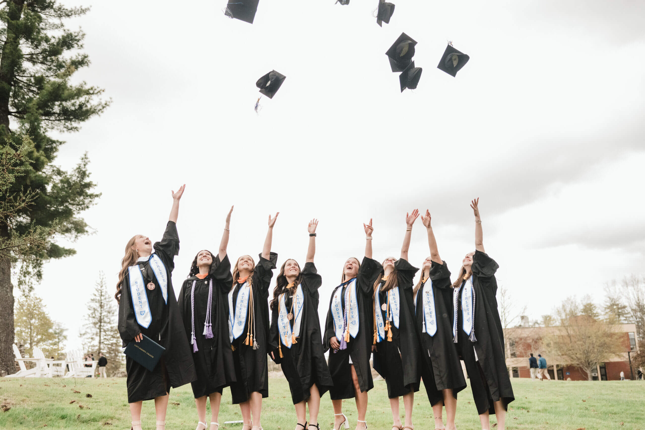 Graduate holding a St. Joseph's College diploma, standing among peers in caps and gowns at the commencement ceremony. Saint Joseph's College of Maine