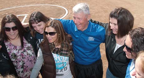 A group of people, including a man in a blue shirt, standing close together on a softball field, smiling and posing for a photo with Dick Bailey. Saint Joseph's College of Maine