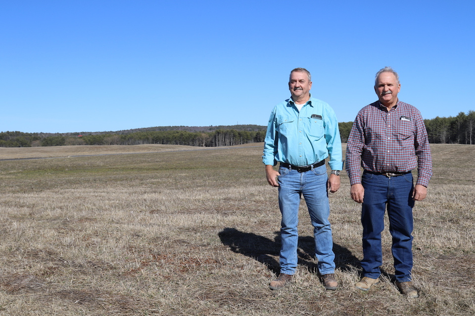 Danny and Jon Shaw stand in a field with blue sky behind.