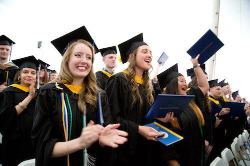 A group of graduates in caps and gowns from Saint Joseph’s College celebrate during the Class of 2018 graduation ceremony; some are clapping and holding their degrees. Saint Joseph's College of Maine