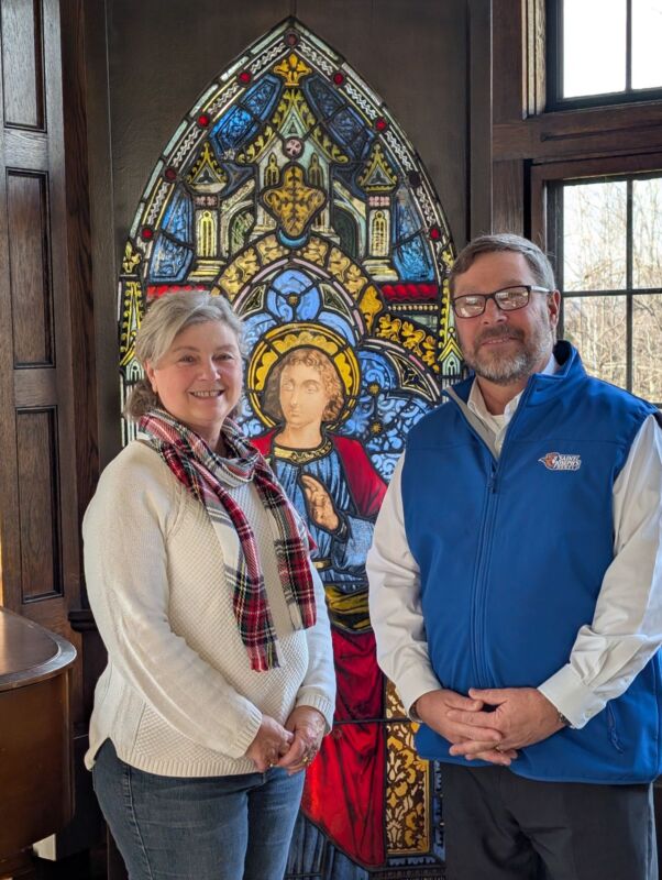 Two people standing in front of a decorative stained glass window featuring a religious figure at Saint Joseph’s College of Maine, capturing the spirit and dedication of nursing students. Saint Joseph's College of Maine
