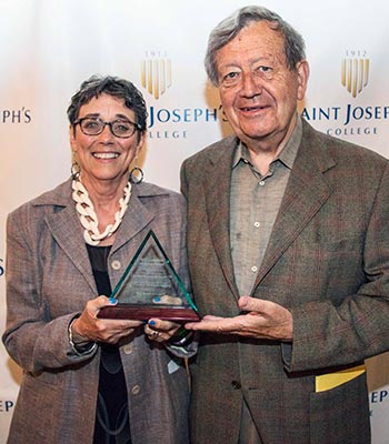 Two people stand together holding the prestigious Catherine McAuley Award. They are posing in front of a step-and-repeat backdrop displaying "Saint Joseph's College. Saint Joseph's College of Maine