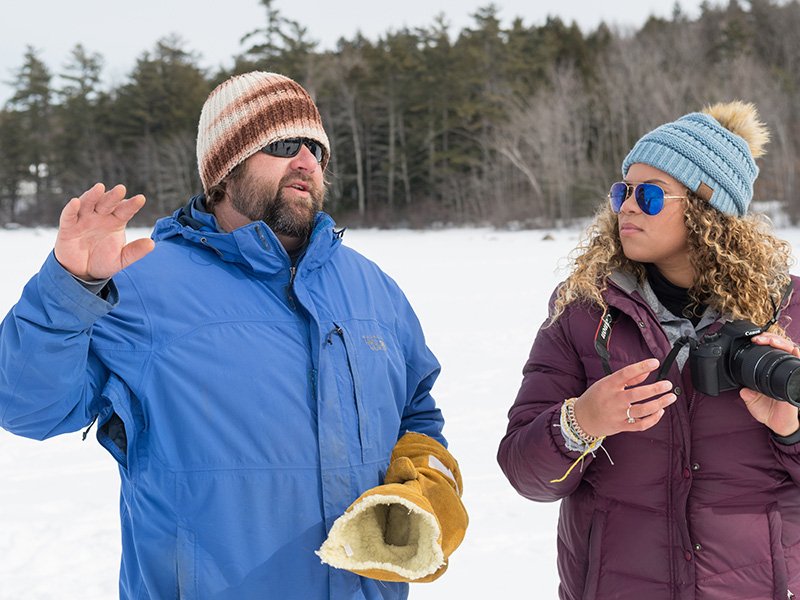 Professor Scott Fuller instructs a photography student during an outside digital photography class on a frozen Sebago Lake.