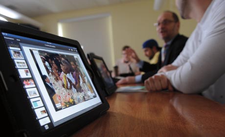 A group of people sit at a conference table with iPads in front of them, one showing a presentation with an image of a child. Saint Joseph's College of Maine