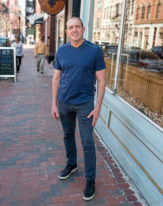 Lee Kennedy poses in a blue shirt on a city street