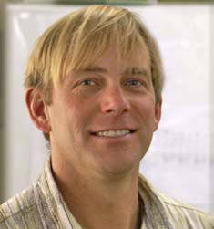 A man with short blond hair, wearing a striped shirt, is smiling confidently. His expression suggests a certain expertise, even as he stands in front of a blurry background. Saint Joseph's College of Maine
