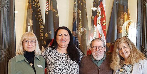 Four adults stand in front of various flags at the Maine State House, smiling at the camera. Two women are on the left and right, and a woman and a man are in the middle. It’s a cheerful group shot celebrating Nurses Day. Saint Joseph's College of Maine