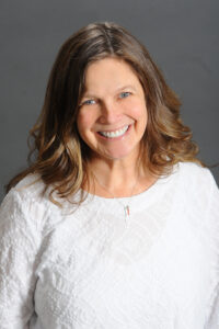 Counseling Center 1 A woman with wavy light brown hair smiles warmly at the camera. She is wearing a textured white top and a necklace with a small pendant, set against a plain gray background. Saint Joseph's College of Maine