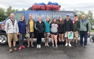 A group of ten people standing in front of a van loaded with gear on the roof. The van has "Saint Joseph's" written on it. The individuals, part of the Environmental Science Semester 2018, are dressed in casual outdoor clothing. Saint Joseph's College of Maine