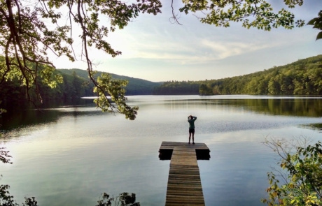 Effie stands on a dock over water, surrounded by trees