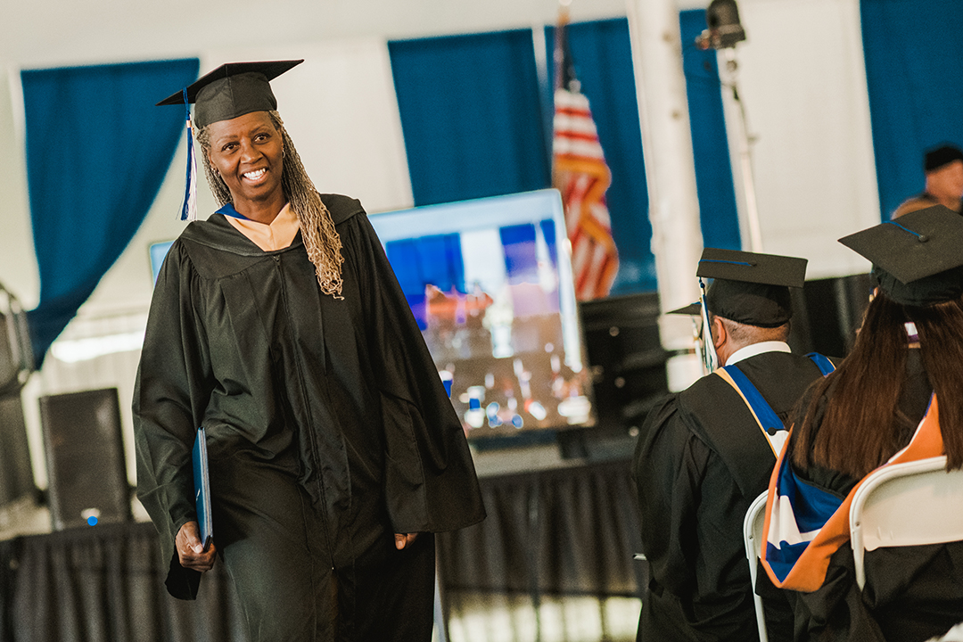 An online graduate walks back to her seat after receiving her diploma.
