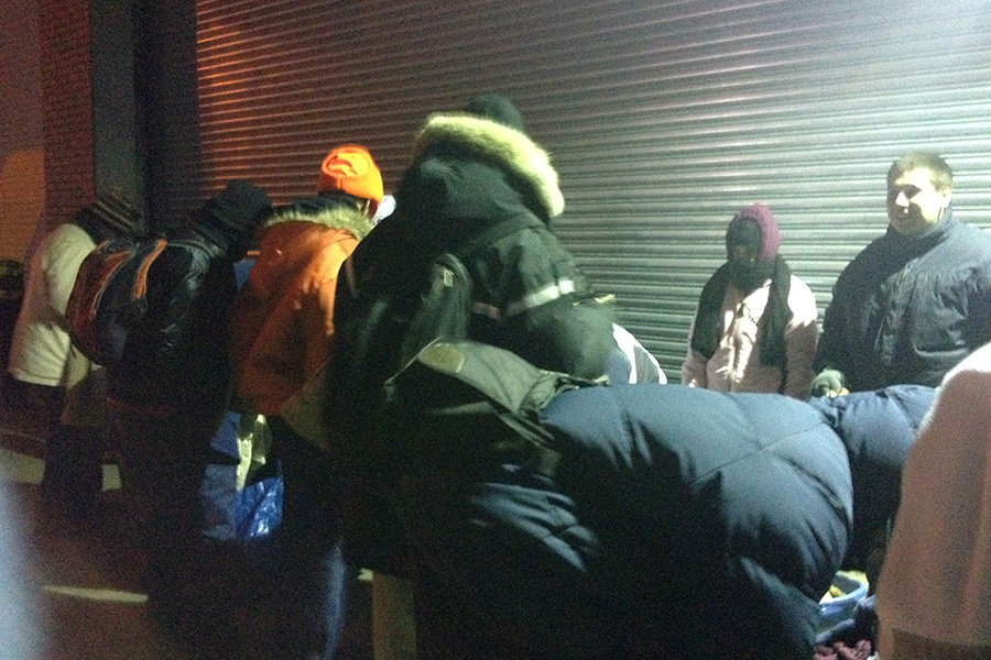 Midnightrun A group of people in warm clothing stand and lean over, facing away from a metallic roller door by the Mercy Center. It appears to be nighttime, hinting at their commitment to community service. Saint Joseph's College of Maine