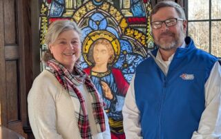 Two people standing in front of a decorative stained glass window featuring a religious figure at Saint Joseph’s College of Maine, capturing the spirit and dedication of nursing students. Saint Joseph's College of Maine