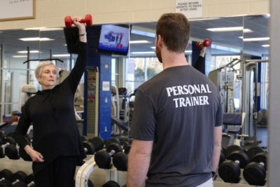 Tommy looks on as Mary Lynn lifts an exercise weight over her head