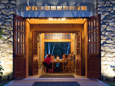 Agritourism A group of people sitting around a table, dining inside a well-lit, open stone building with large wooden doors, at twilight; their meal provided by the Institute for Local Food Systems Innovation. Saint Joseph's College of Maine