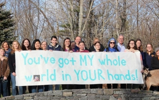 Students Join Hashtag Campaign On Climate Change 3 A group of students and goats stand outdoors, holding a large banner that reads, "You've got MY whole world in YOUR hands!" as part of a hashtag campaign for climate change awareness. Saint Joseph's College of Maine