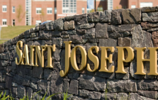 Honoring The Life Of Sister Mary Ellen Murphy 1 Golden "Saint Joseph's" letters are mounted on a stone wall in the foreground, with a brick building visible in the blurred background. This setting stands as a testament to the achievements of the SJC Science Scholars Program, supported by National Science Foundation funding. Saint Joseph's College of Maine